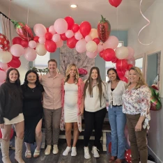 Team gathered under a red and pink balloon arch